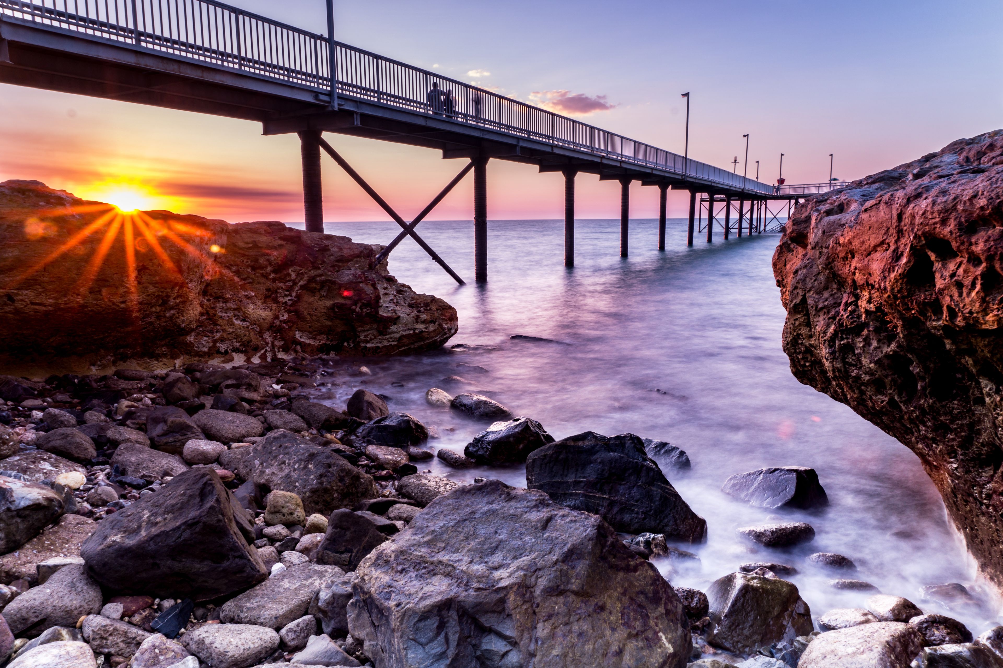 Un pont en bord de mer, avec un coucher de soleil en arrière-plan.
