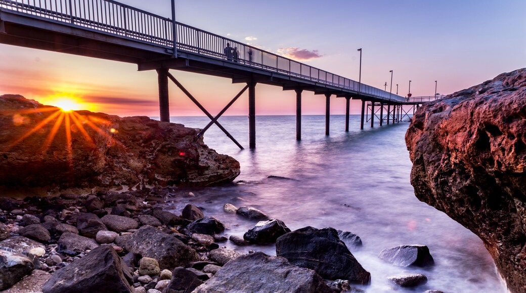 Un pont en bord de mer, avec un coucher de soleil en arrière-plan.