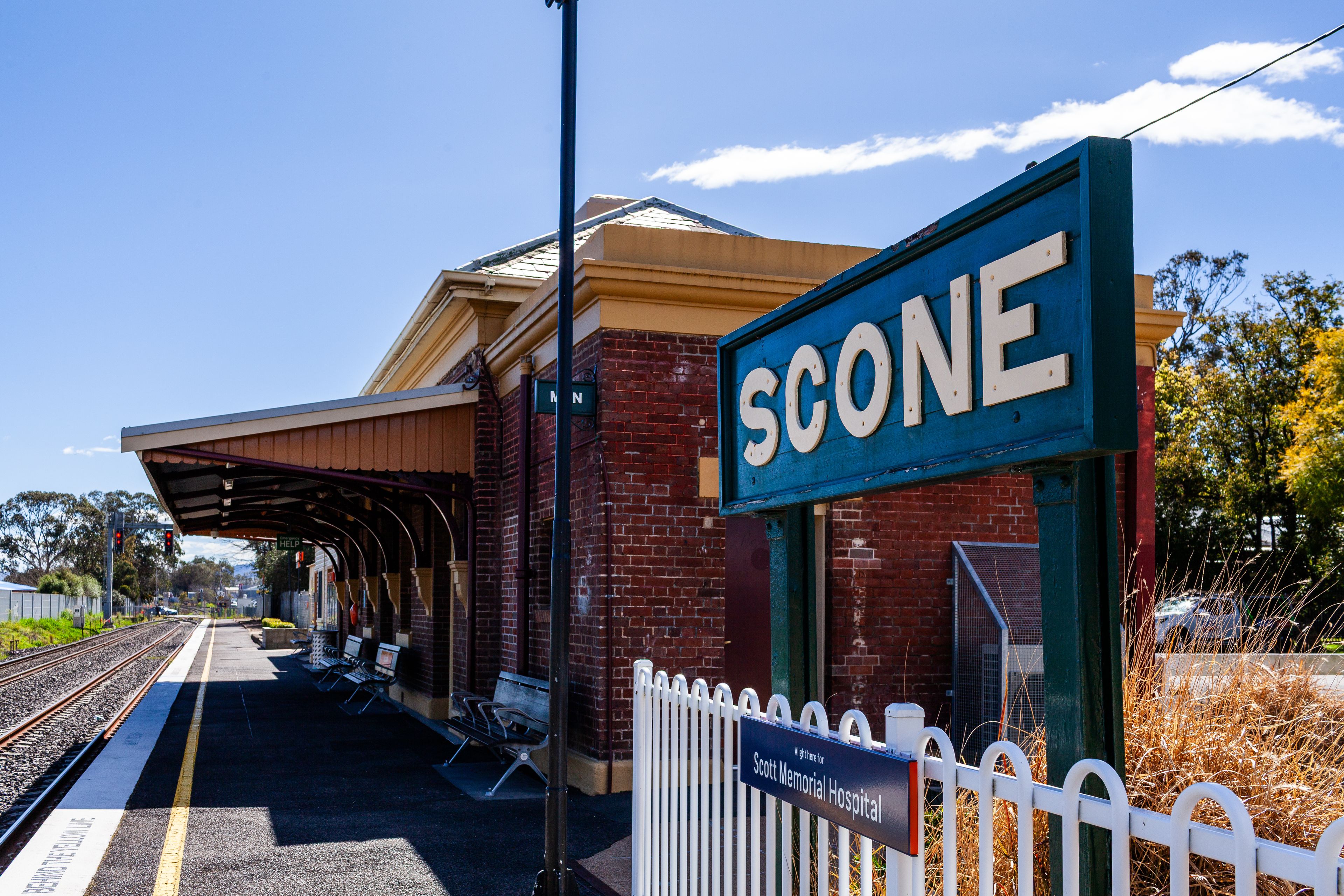 Une plateforme de gare avec une pancarte indiquant « SCONE » et, au premier plan, une autre pancarte indiquant « Scott Memorial Hospital ».