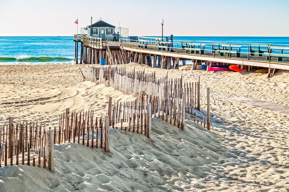 A beach with wooden groynes, a pier, and a lifeguard tower.