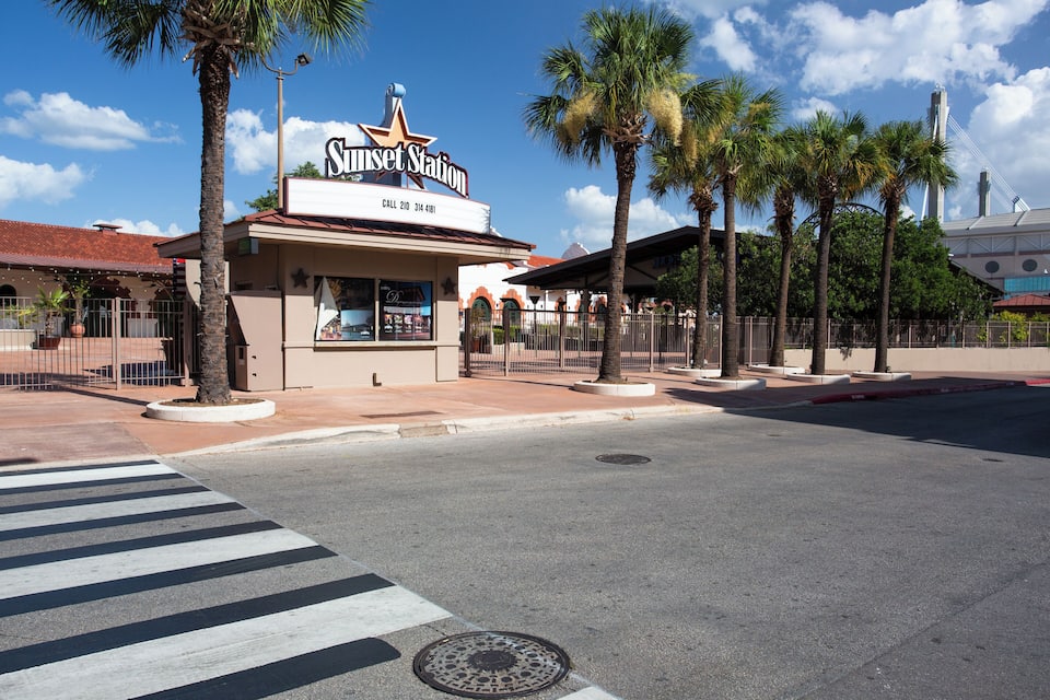 A street with a Sunset Station sign, palm trees, and a clear blue sky.
