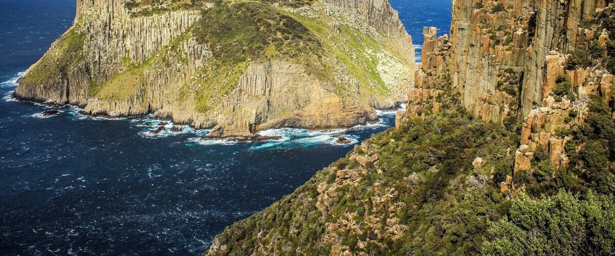 A coastal cliff with a lighthouse, rugged terrain, and a steep drop-off into the ocean.