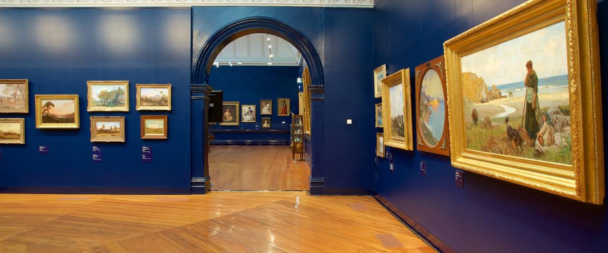 An art gallery with wooden floors and blue walls, featuring various framed paintings.