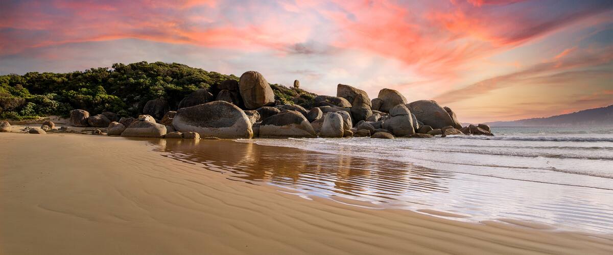 Une plage avec de gros rochers et un ciel au coucher du soleil.