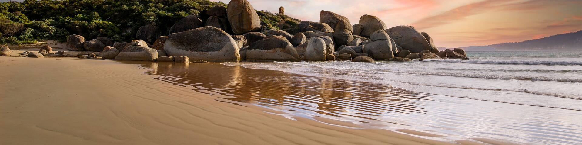 A beach with large rocks and a sunset sky.