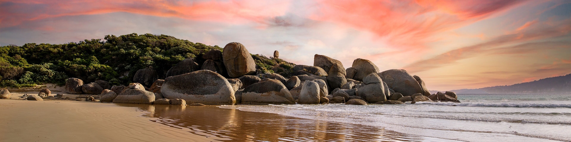 Uma praia com pedras grandes e um céu ao pôr do sol.