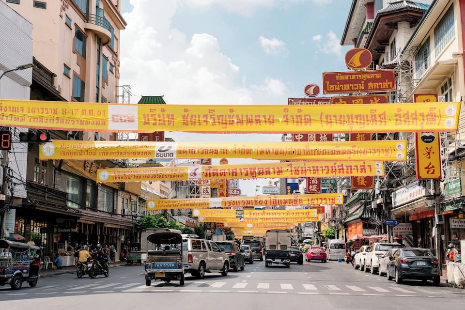 A busy street with yellow banners and signs in a foreign language, vehicles, and buildings.