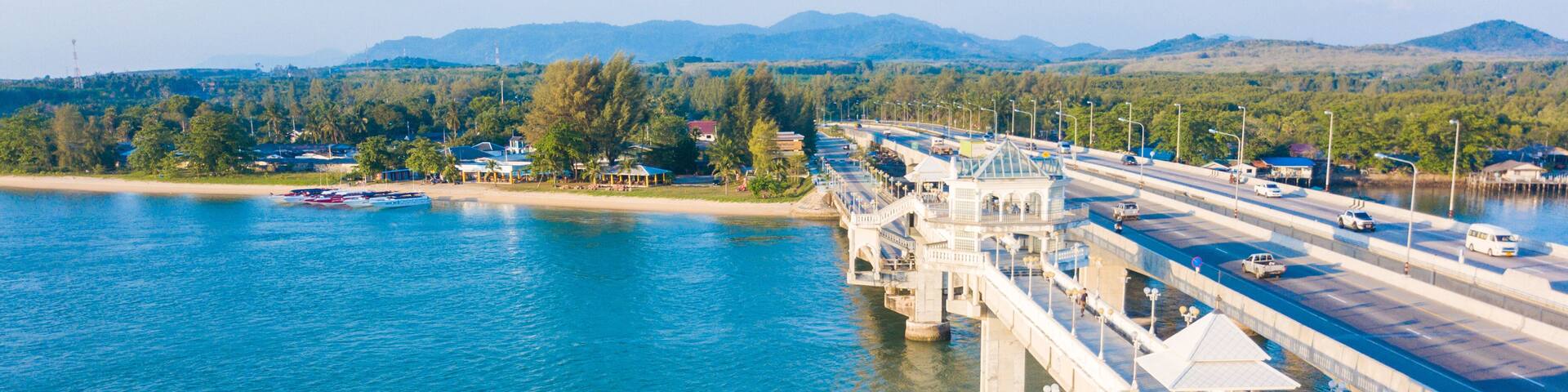 A bridge over a river with boats, a pedestrian walkway, and distant mountains.