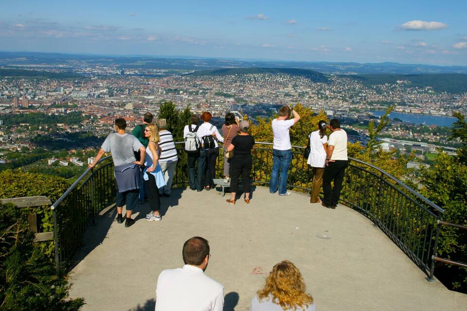 Un grupo de personas en una plataforma de observación con vistas a un paisaje urbano, un río y colinas a lo lejos.