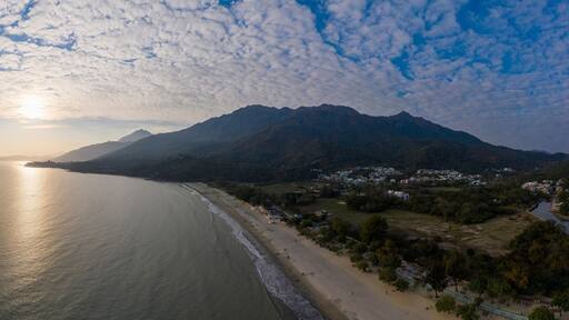 Paisaje costero con playa, montañas y una masa de agua que refleja el sol.