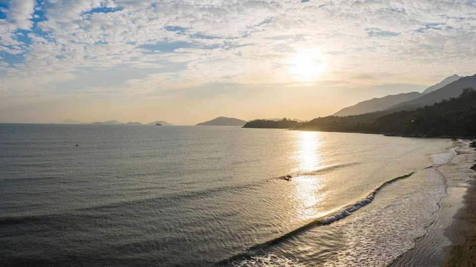 A beach with a calm sea, a clear sky, and mountains in the background.
