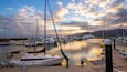 A marina with various boats docked, a clear sky, and mountains in the background.