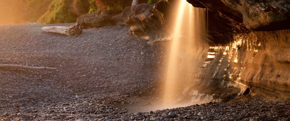 A waterfall flowing over rocks into a river surrounded by trees.