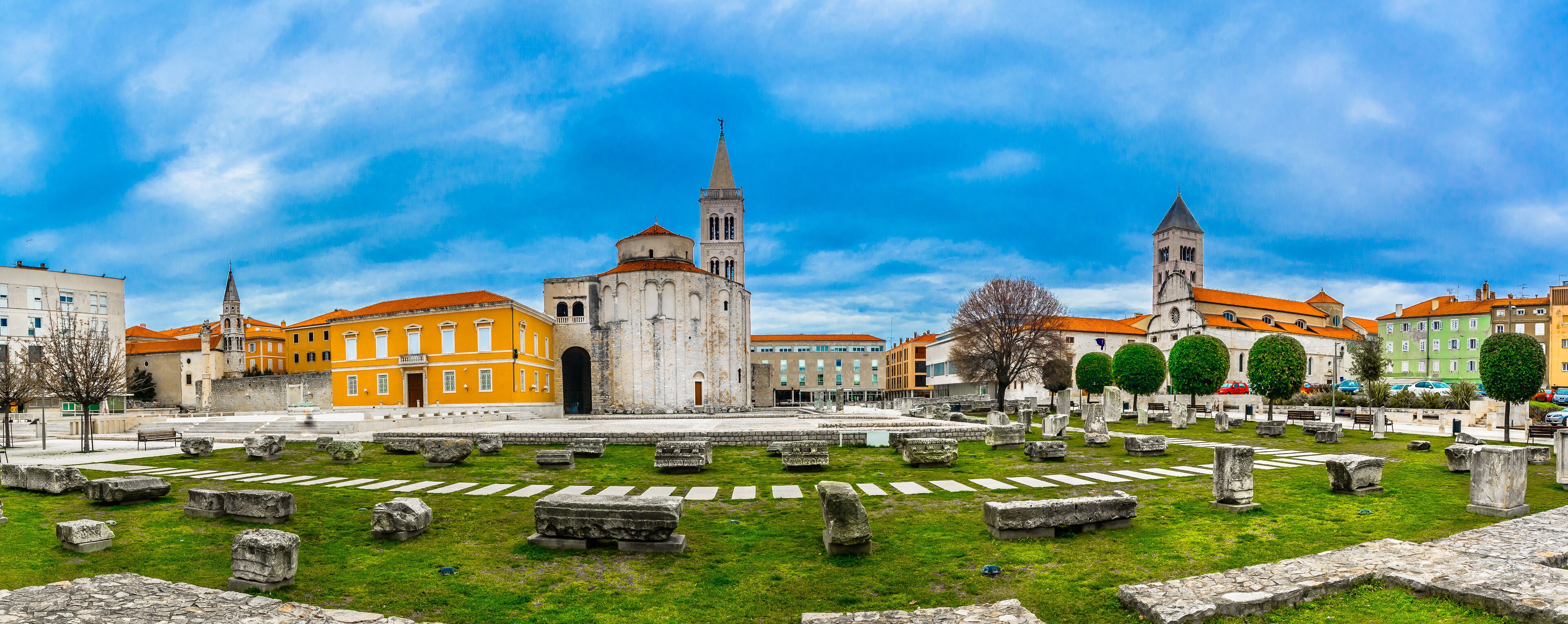 A historic square with ancient ruins, a prominent church, and a tall tower.