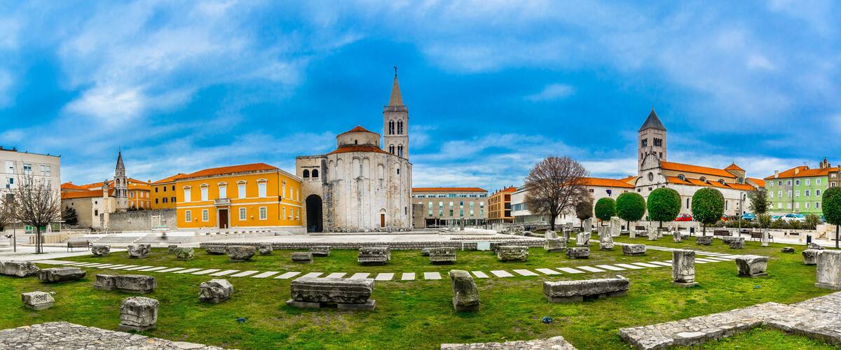 A historic square with ancient ruins, a prominent church, and a tall tower.