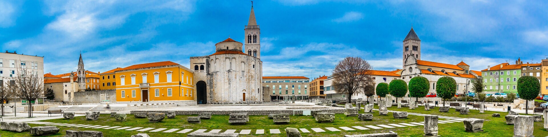 A historic square with ancient ruins, a prominent church, and a tall tower.
