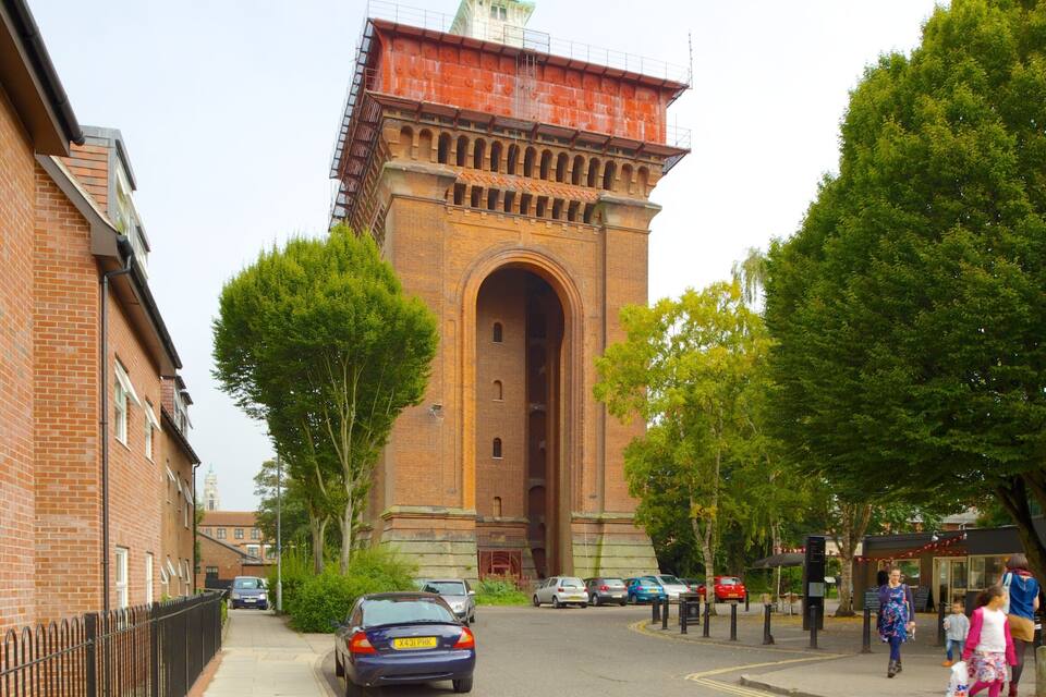 A brick building with a large archway, surrounded by trees and parked cars.
