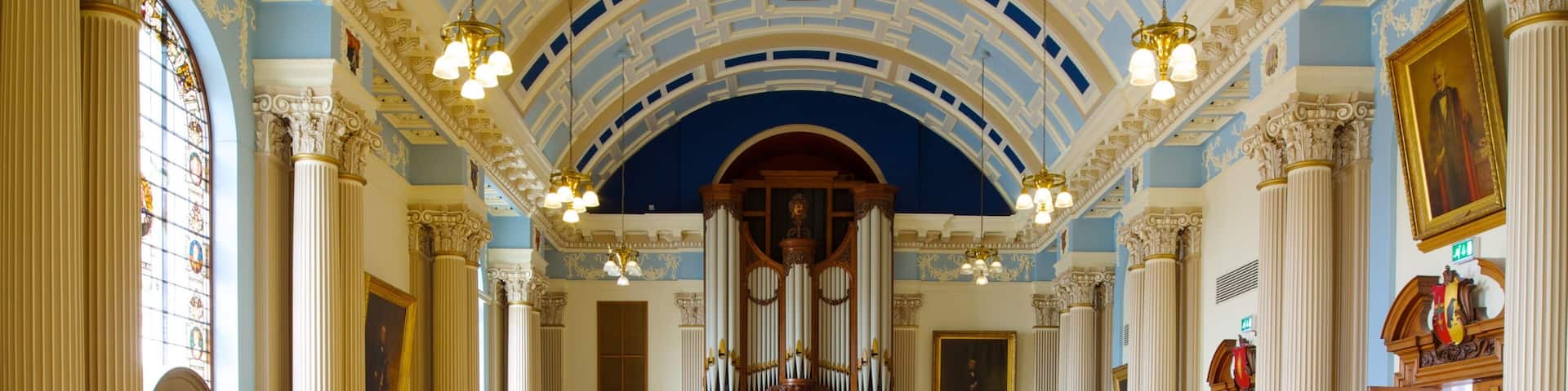 A grand hall with ornate columns, a large organ, and a high, blue ceiling.
