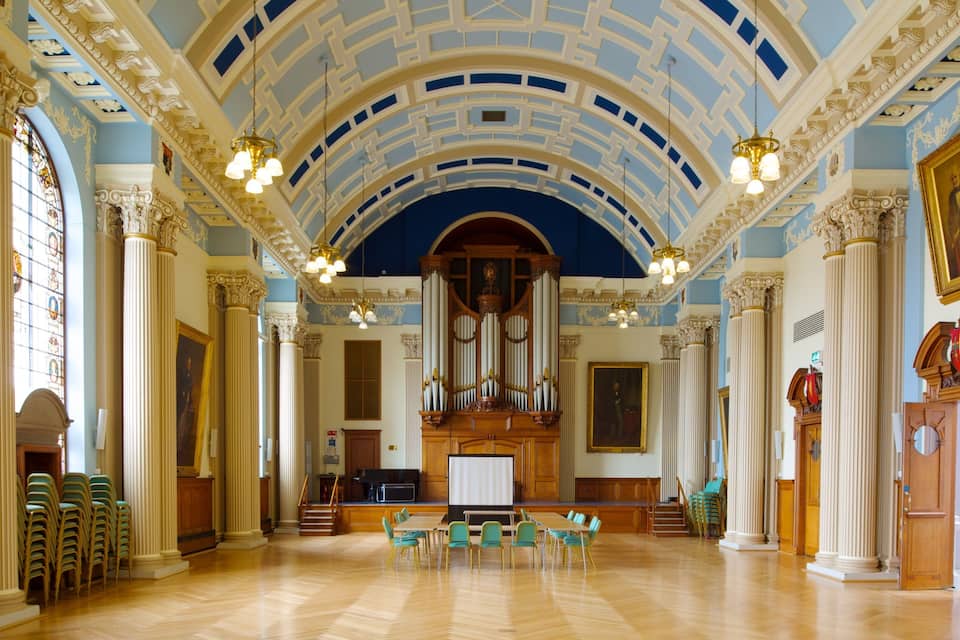 A grand hall with ornate columns, a large organ, and a high, blue ceiling.