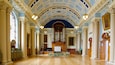 A grand hall with ornate columns, a large organ, and a high, blue ceiling.