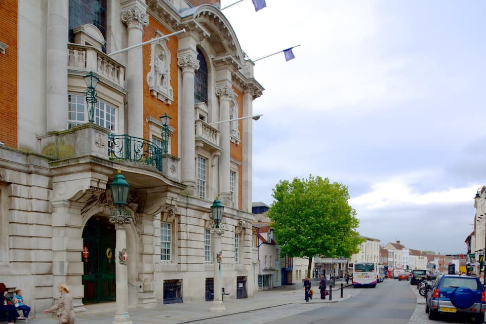 A historic building with ornate architecture, a tree-lined street, and a bus in the background.