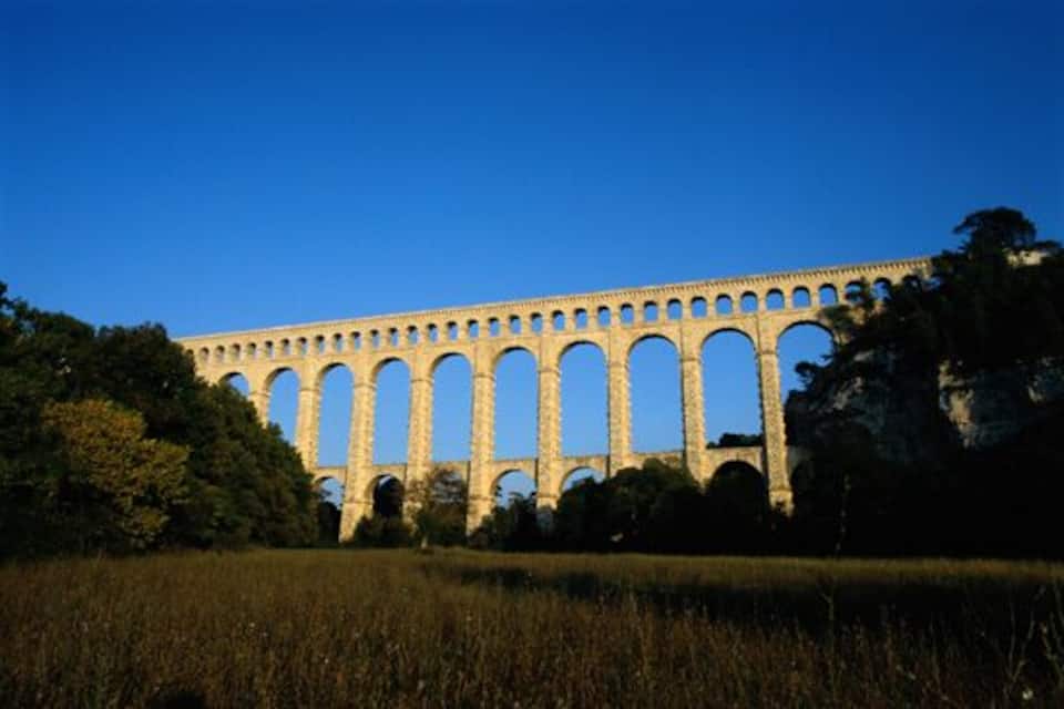 A large stone viaduct with multiple arches, surrounded by trees and grass.