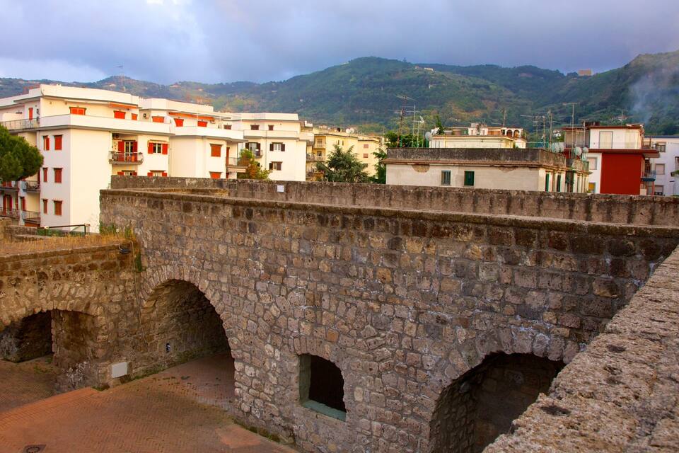 A stone bridge with arches, a stone wall, and buildings in the background.
