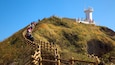 A wooden staircase leading up a hill with a lighthouse at the top.