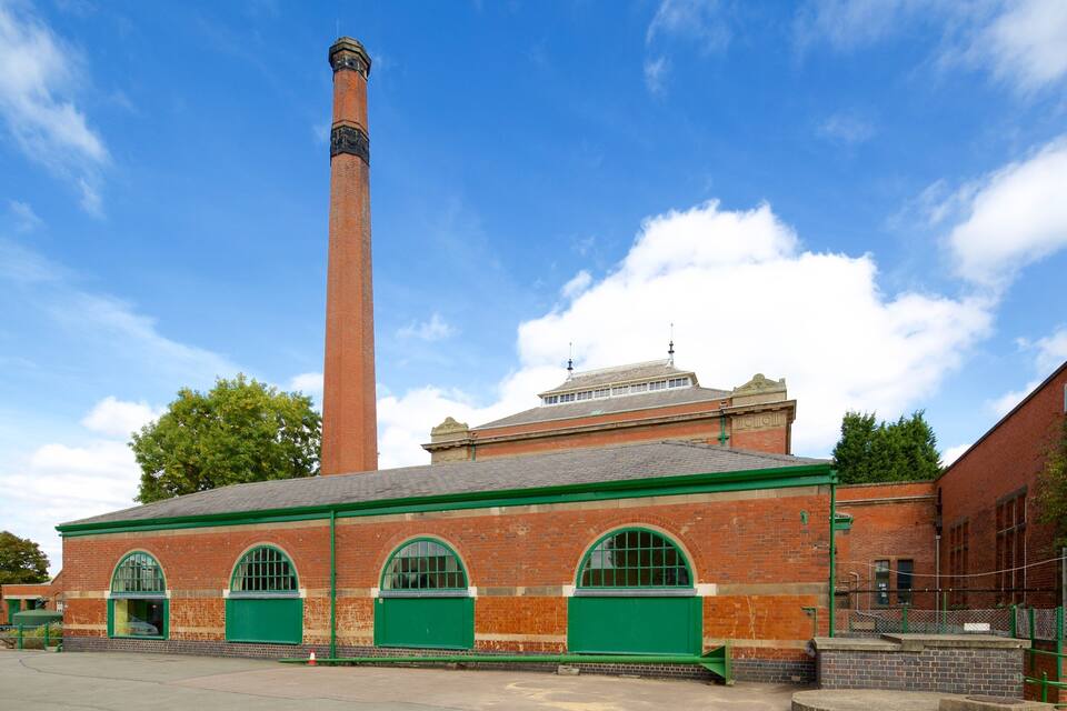 Un edificio de ladrillo con una chimenea alta, puertas verdes y ventanas arqueadas.