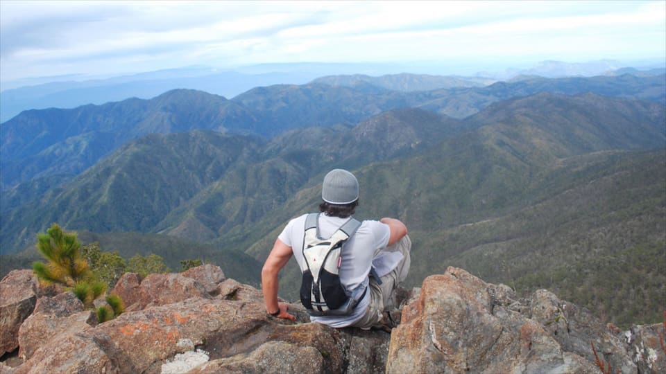 A hiker sitting on a rocky outcrop overlooking a mountainous landscape.