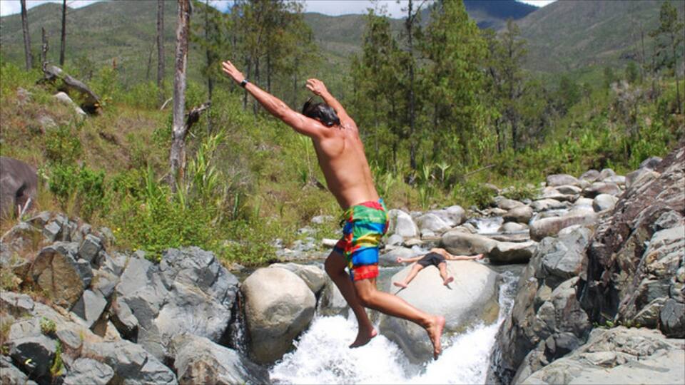 A man jumping off a rocky waterfall in a forested area.