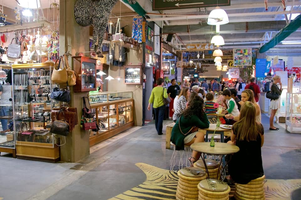 A busy indoor market with various stalls selling handbags, jewelry, and other items.