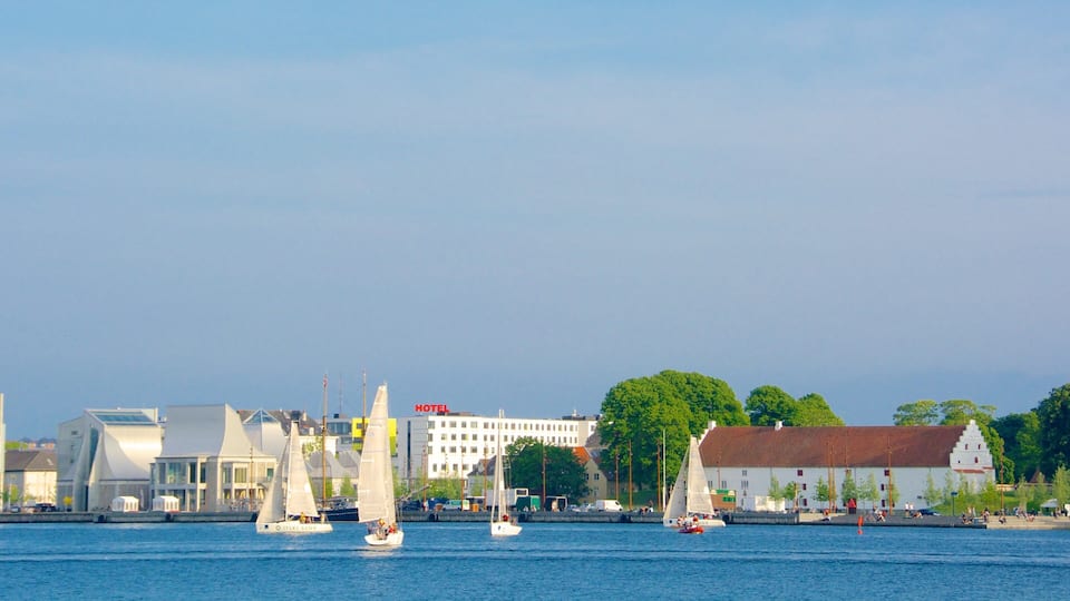 Sailboats on a calm river, a modern building with a 'HOTEL' sign, and a traditional building with a red roof.