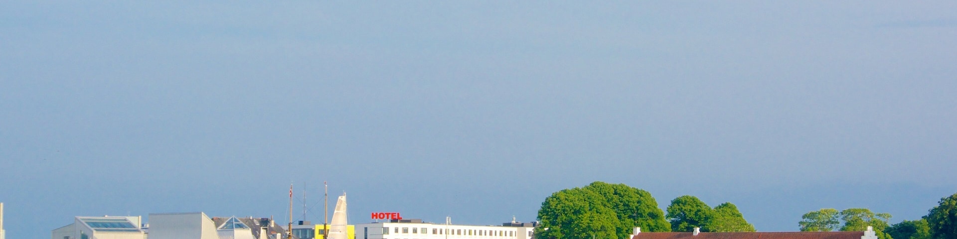 Sailboats on a calm river, a modern building with a 'HOTEL' sign, and a traditional building with a red roof.