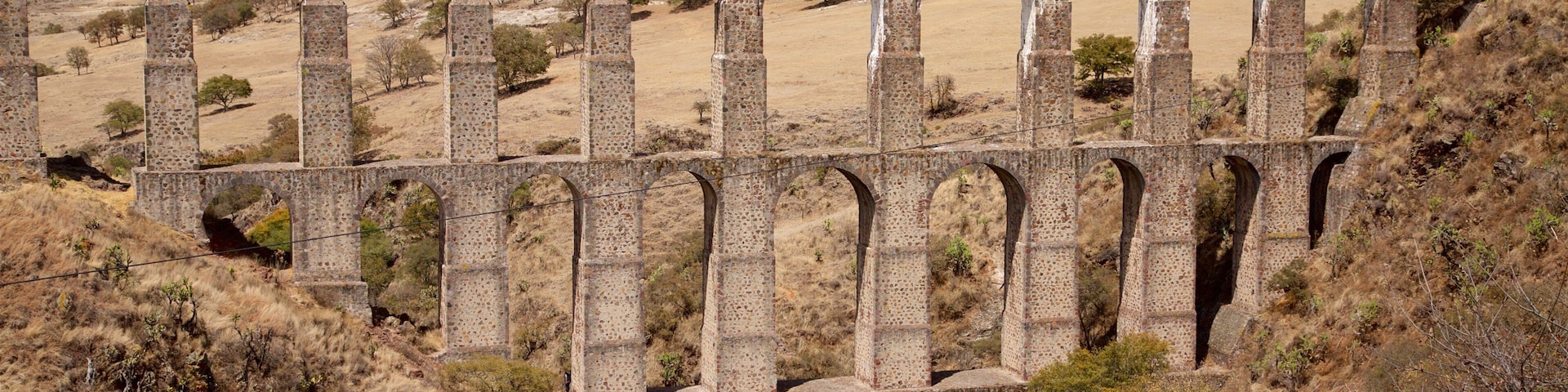 Um viaduto de pedra com várias abóbadas atravessa uma paisagem seca e montanhosa.