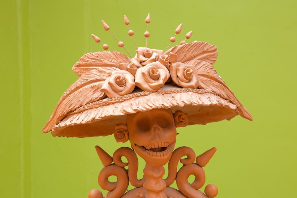 Uma escultura de caveira com um chapéu grande adornado com flores e folhas.