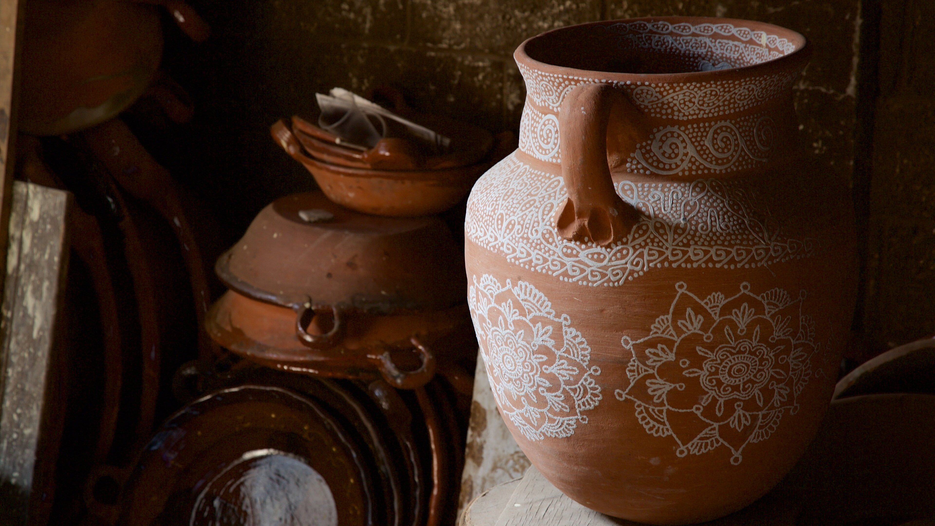 A large clay pot with intricate white patterns, stacked with other pottery items.