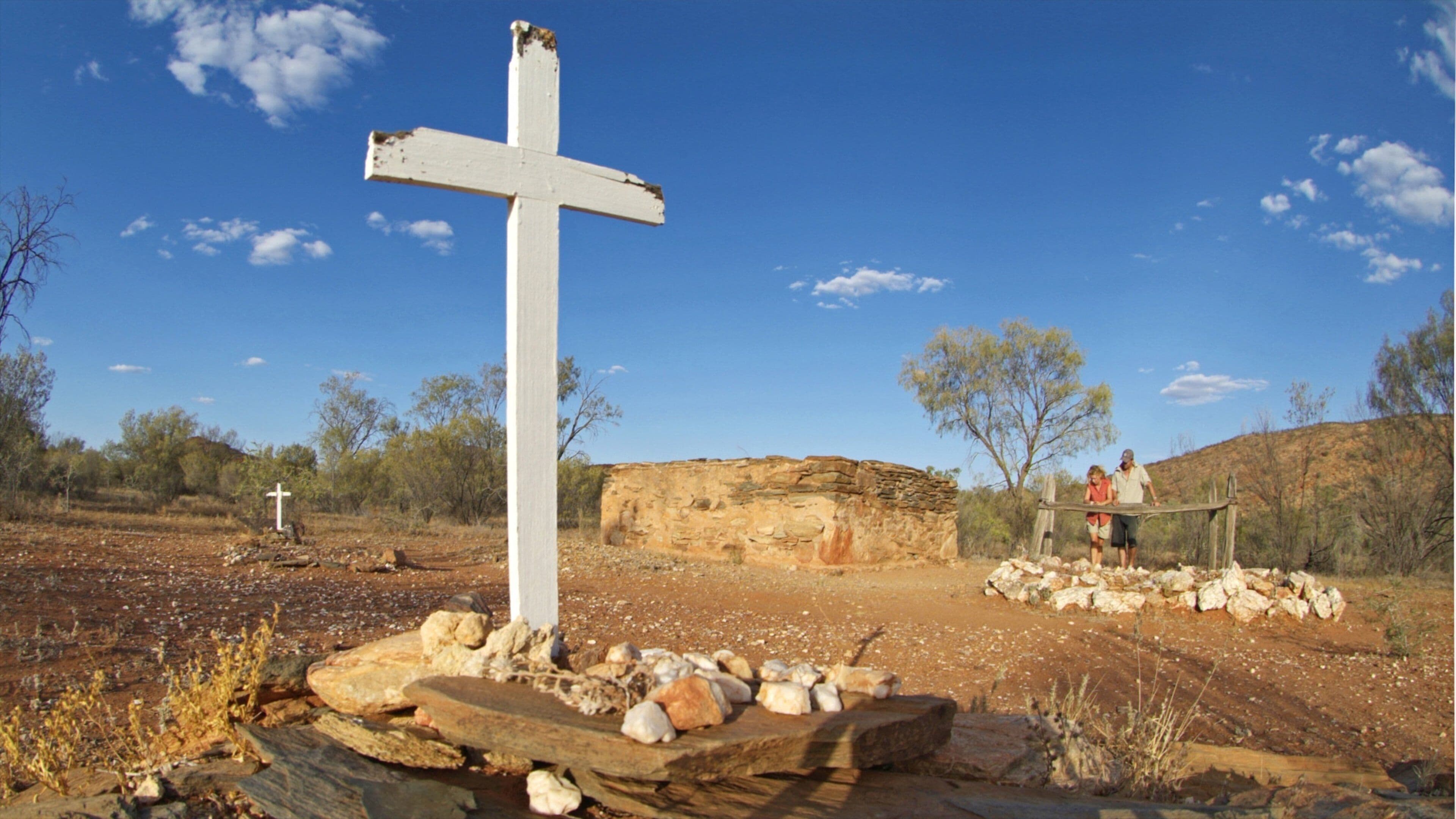 A white cross in a desert landscape with rocky terrain and sparse vegetation.