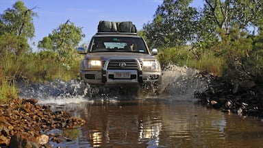 A Toyota SUV crossing a shallow stream with rocks on the banks.