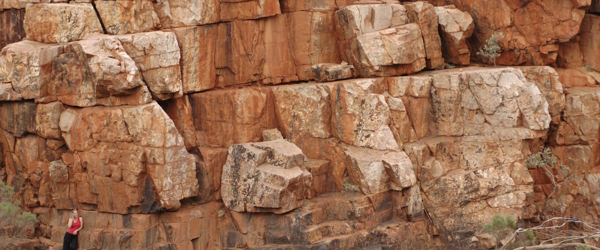 A rocky cliff with a person sitting on a ledge and another person standing nearby.
