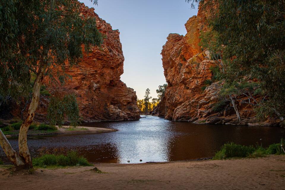 A river flowing through a canyon with red rock walls and trees on either side.