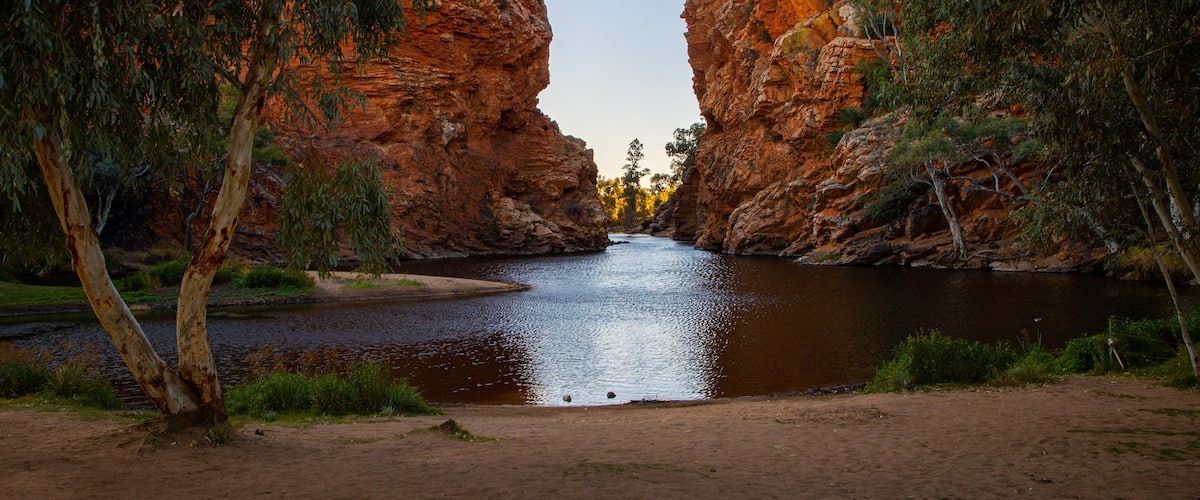 A river flowing through a canyon with red rock walls and trees on either side.