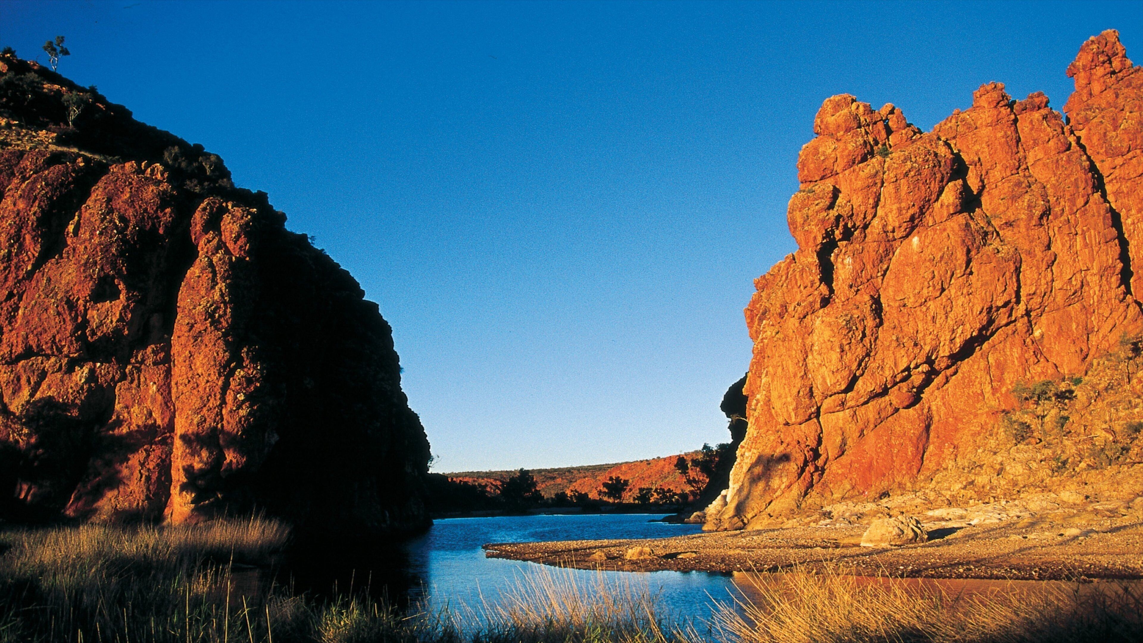 A river canyon with red rock formations and a clear blue sky.