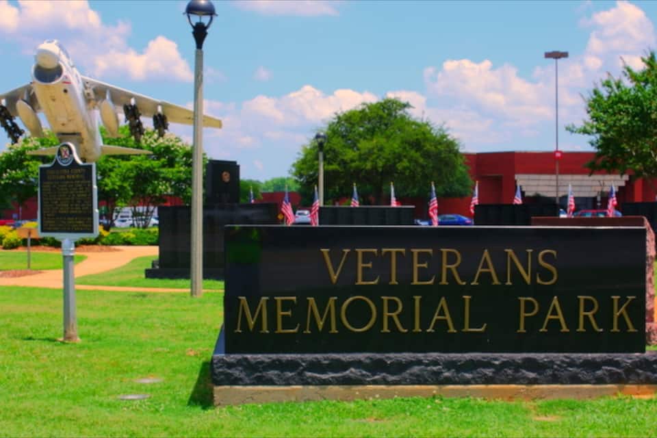 Letrero del Parque Memorial de Veteranos con un modelo de avión y banderas.