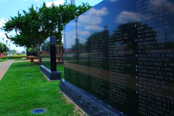 A memorial wall listing names of individuals, surrounded by a park with grass and trees.