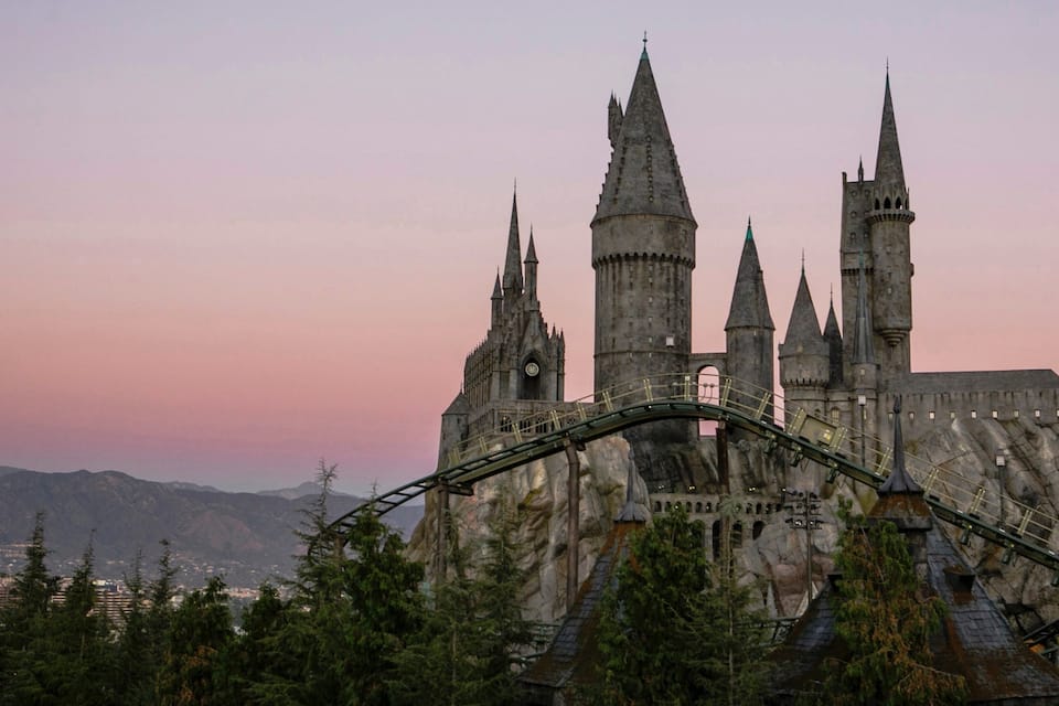 Un castillo con múltiples torres y una montaña rusa al frente.