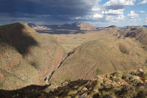 A mountainous landscape with a valley and distant mountains under a partly cloudy sky.