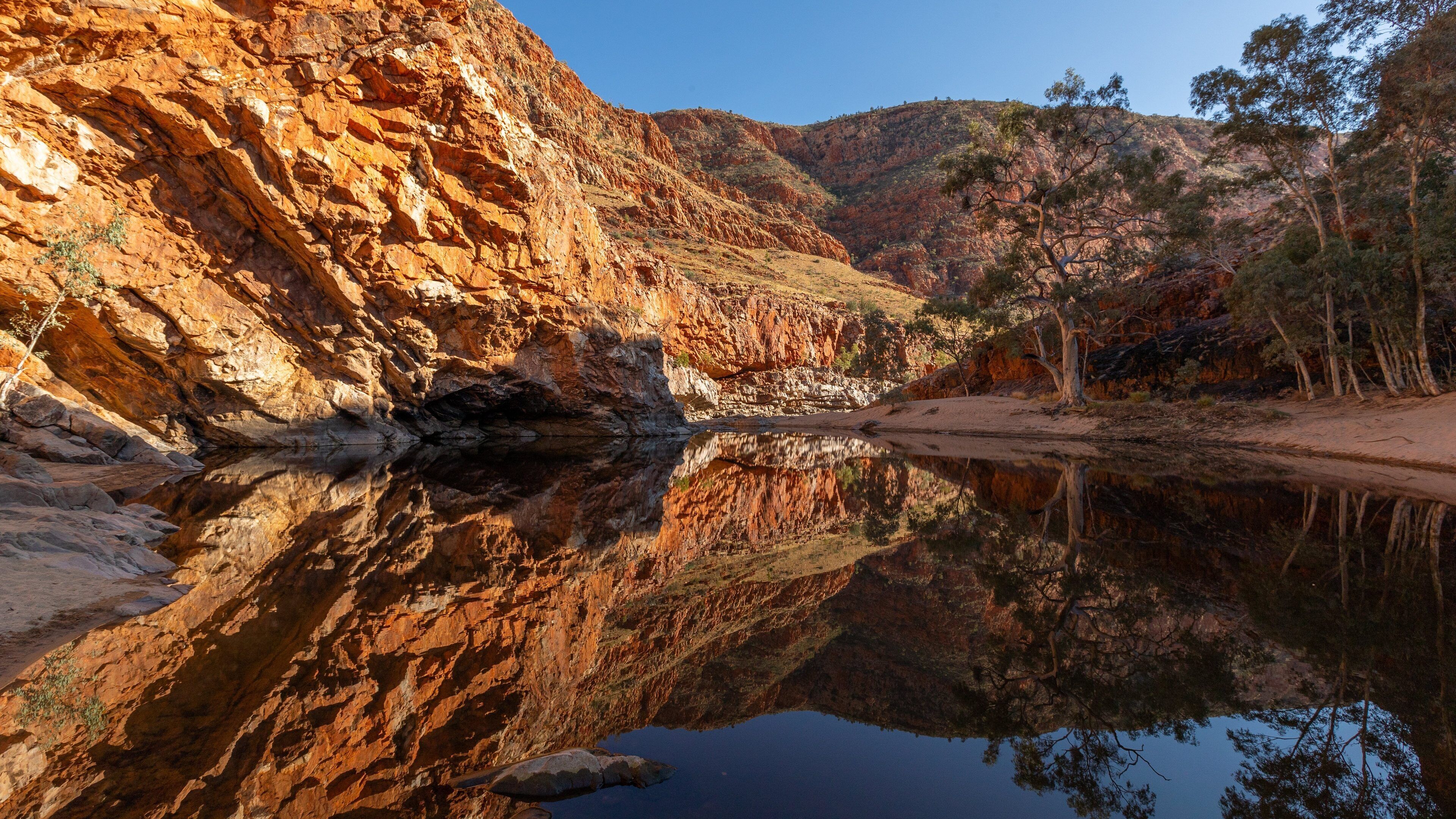 A canyon with red rock formations and a calm river reflecting the scenery.
