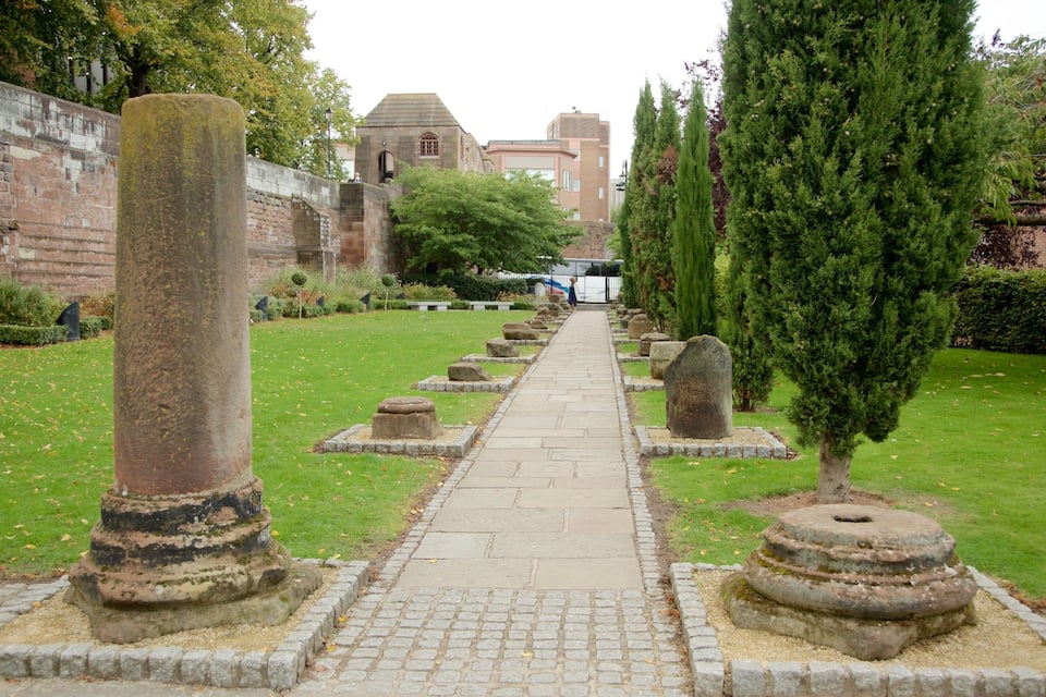 A pathway lined with stone columns and tombstones, leading towards a building with a dome.