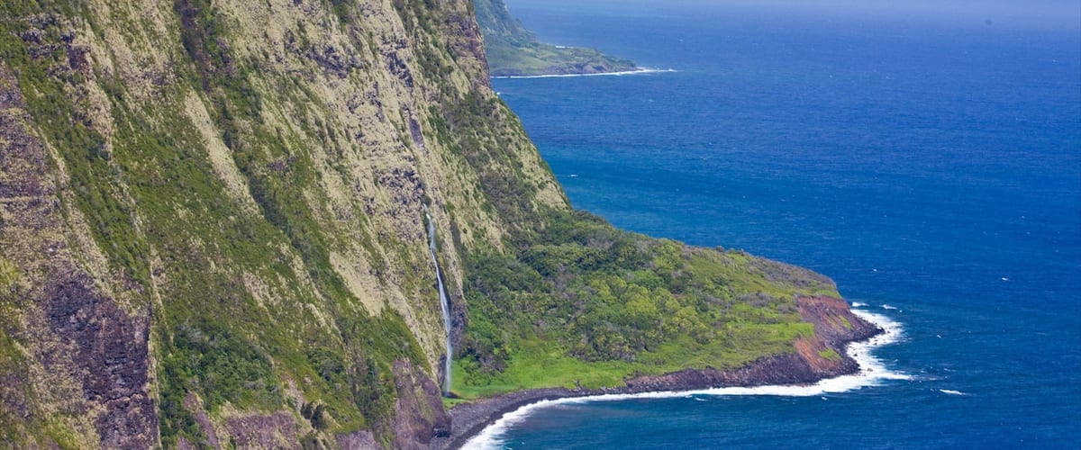 A steep cliff with a waterfall, a coastline, and the ocean.